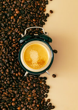 Cup of fresh espresso integrated into a retro alarm clock surrounded by coffee beans on beige background. Creative coffee concept. Morning routine, wake up time and caffeine addiction flat lay idea.
