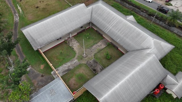 A view from the top of a simple, minimalist-style school building with a U-shaped layout surrounding a grassy courtyard and a flagpole.