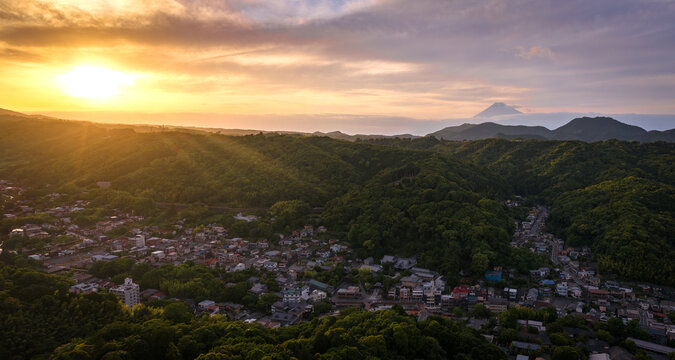 Aerial view of Shuzenji town nestled in the lush green hills of Izu at sunset, with the silhouette of Mount Fuji visible in the distance, Izu, Shizuoka, Japan.