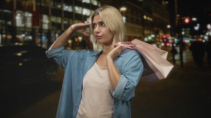 Fototapeta premium Woman carrying shopping bags holds hand to forehead on a city street at night with a pink bag over her shoulder; confidence night out.
