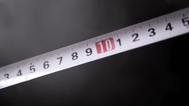 A metal measuring tape extends diagonally across a dramatic dark and smoky background. Concept of exact precision, industrial construction planning, and calculating exact distance.