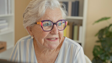 Woman wearing colorful glasses smiles and looks to the side in a building with bookshelves and a desk  serene reflection. © Krakenimages.com
