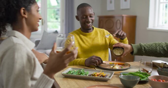 Diverse friends sharing dinner, man sitting at home table getting topping from right bowl