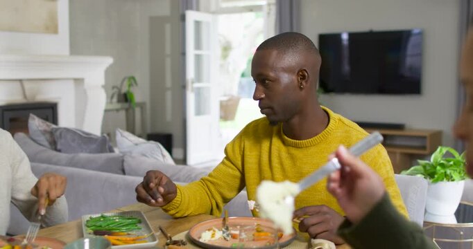 African American family man in gold knit watching spoon offered cutting eating sharing meal at home