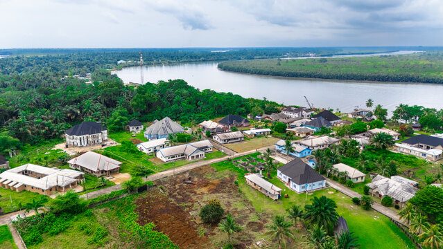 Aerial view of a residential settlement nestled along a riverbank with lush green vegetation, scattered houses, and dirt roads in Minima, Rivers, Nigeria.