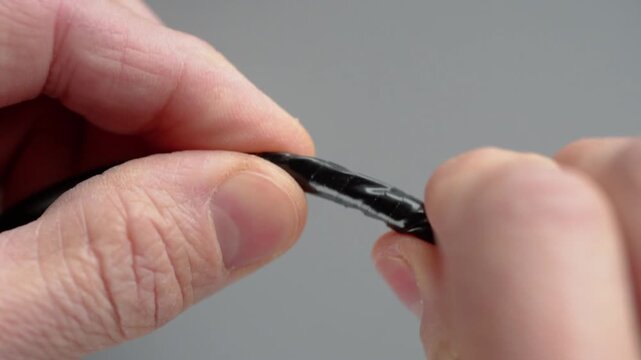 Closeup hands twisting and smoothing tape over small splice on black cable, focused technician action, neat adhesion, tension control and tidy insulation step