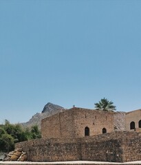 Fototapeta premium `Traditional stone building with palm tree and Al Hajar mountains in Oman`