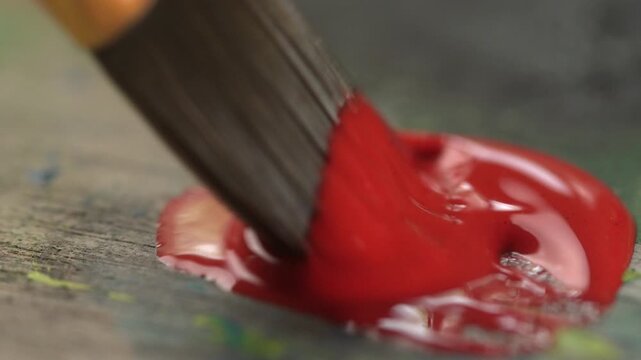 A paintbrush picks up thick acrylic red paint on a wooden palette. Concept: Hobbies and creative processes