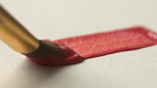 A close-up of a brush leaving a red line on white paper. The process of brush movement and paint texture during the creation of a drawing. Hobbies and leisure concepts