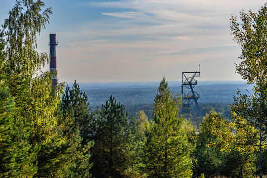 The steel shaft tower and chimney of the abandoned Boże Dary mine, surrounded by trees. View from the Kostuchna slag heap. Katowice, Silesia, Poland