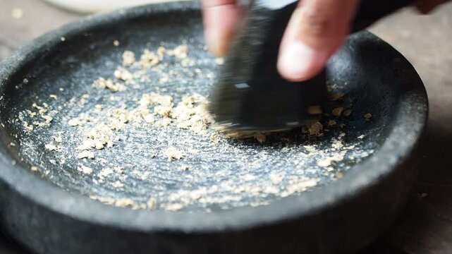 Close-up of hand grinding dry ingredients in a traditional stone mortar with a pestle for food preparation