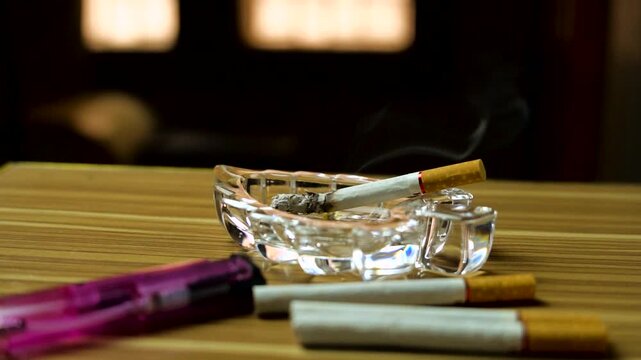 Lit cigarette burning in a crystal ashtray with lighter smoke smoking tobacco ash pink smoke smoking tobacco ash pink