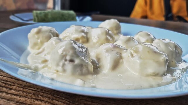 Savory meatballs are served smothered in a thick white cream sauce on a light blue plate. Concept of comfort food, hearty lunch, Scandinavian cuisine, and delicious homemade cooking.