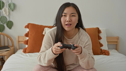 Woman holding a game controller, hands gripping the controller on a bed in a bedroom  focused concentration. © Krakenimages.com