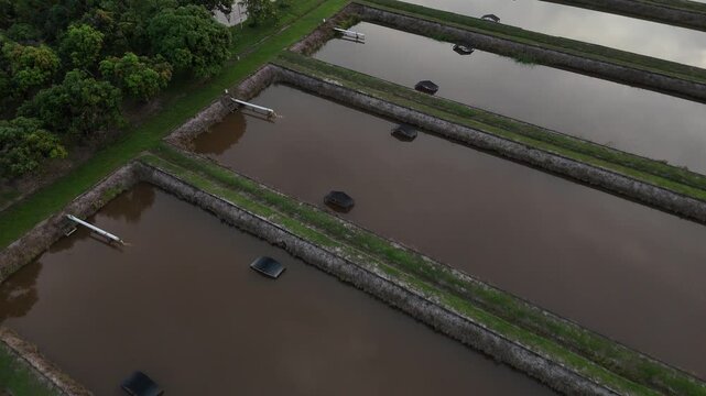 A view from above a rectangular fish farm pond equipped with drainage pipes and embankments.