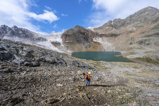 Mountaineer on a hiking trail, mountain landscape with limestone rocks between granite mountains, mountain lake Hinterer Senner Egetsee and mountain peak of the Moarer Wei&szlig;en, Seven Lakes Hike, Stubai Alps, near Ridnaun, South Tyrol, Italy