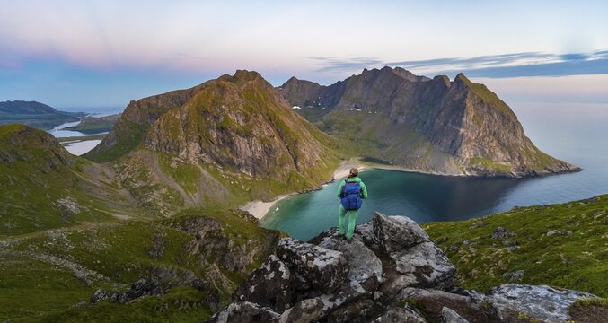 Hiker on top of Ryten, sea, Kvalvika beach and mountains, Fredvang, Lofoten, Nordland, Norway