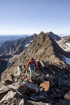 Mountaineer on a rocky ridge, ascent to the Wilder Freiger mountain peak, behind her the summit of the Becher with Becherhaus, picturesque high mountain landscape, Stubai Alps, South Tyrol, Italy