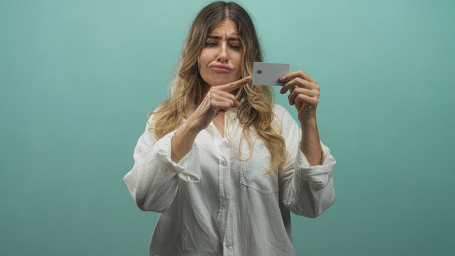 Woman points finger to creditcard while holding card against teal studio wall; frustration mistrust.
