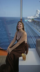 Obraz premium Woman smiling and sitting showing cleavage on cruise ship terrace with ocean view and drink nearby; relaxed serenity.