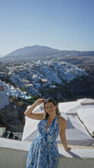 Obraz premium Woman raising arm with sunglasses on a white building terrace, leaning on a wall and smiling at the view; vacation serenity.