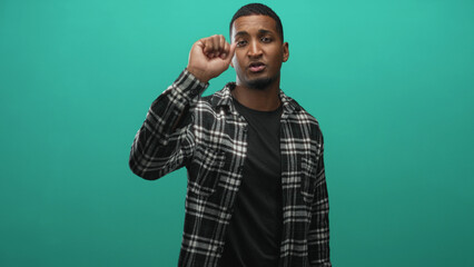 Naklejka premium Young black man holding electric screwdriver in right hand while speaking and gesturing toward camera in a studio with teal backdrop; practical confidence.