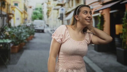 Fototapeta premium Woman cupping hand to ear and pointing at chest on a narrow sunlit street; curiosity attentive friendly.