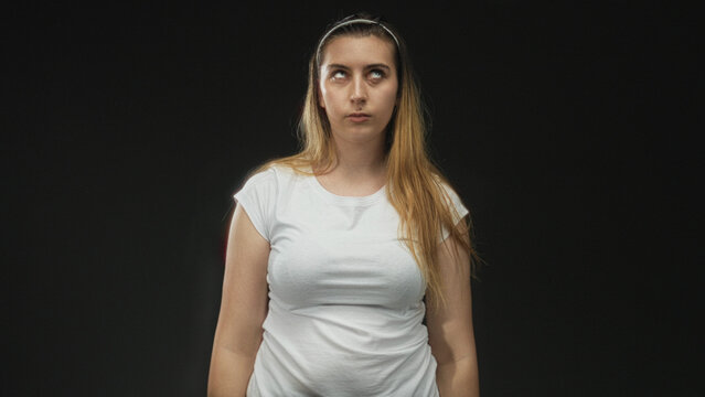 Woman rolling eyes in studio wearing white tshirt and headband, standing with unimpressed stare; annoyance silent critique.