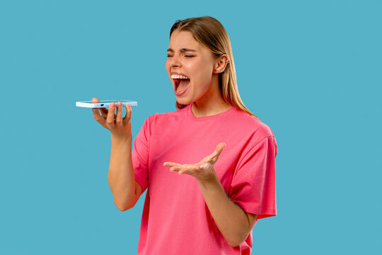 Annoyed Young Woman Quarreling Talking On Mobile Phone.Angry Lady On Blue Studio