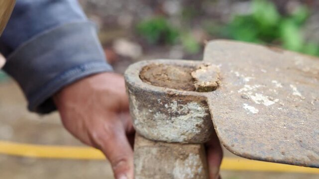 Man repairing old garden hoe with hammer and wooden wedge, close-up of hands