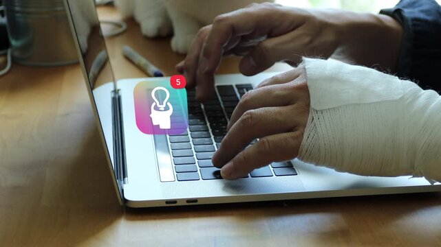 Close up of an injured Asian man with a bandaged arm typing on a laptop, with a 3D tracked human profile lightbulb spark genius idea notification pop up and red counter.