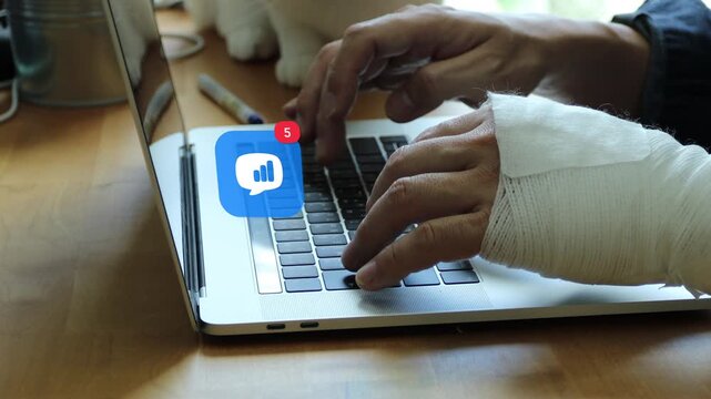 Hands of an injured East Asian man with a white bandage typing on laptop, showing a 3D tracked speech bubble business bar chart analytics notification pop up and red counter.