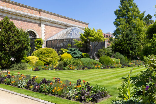 Sunlit Herbgarden (Kruidtuin) in Leuven, Belgium with historic greenhouse, formal lawn and colorful flower beds