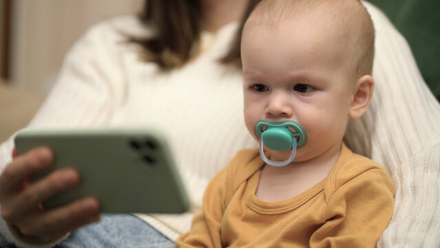 mom holding a cute little baby in her arms and watching cartoons on a smartphone