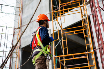 Construction worker wearing a safety harness while working on scaffolding at a building site.