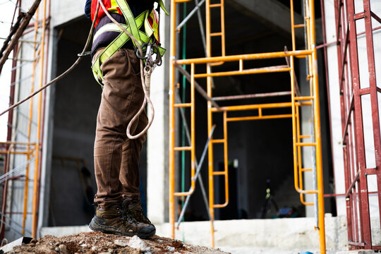 Close-up of construction worker wearing safety boots and harness at a building site.
