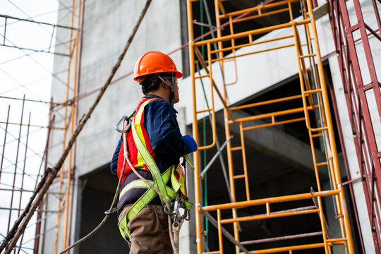 Construction worker wearing a safety harness while working on scaffolding at a building site.