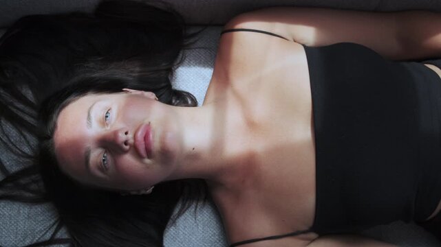 Young beautiful woman with blue eyes lying on sofa in soft sunlight, calm reflection and peaceful thinking at home interior