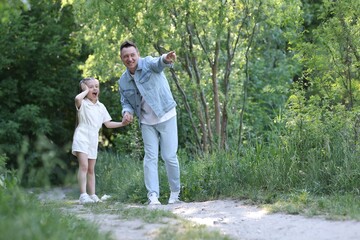 Fototapeta premium Smiling father pointing at something to his surprised daughter outdoors. Space for text