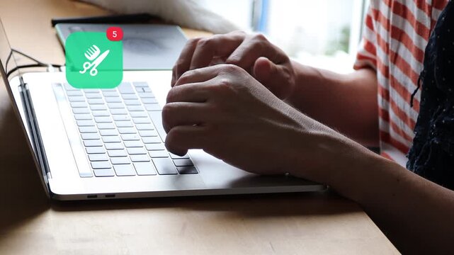 Close up of an Asian man hands typing on a laptop keyboard in casual wear, displaying a 3D tracked barber hair salon comb scissors notification pop up and red counter.