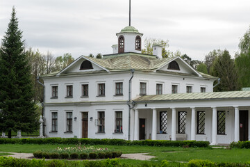 Naklejka premium Historic white mansion features a green roof and decorative windows, set amidst lush greenery and trees in a tranquil outdoor environment