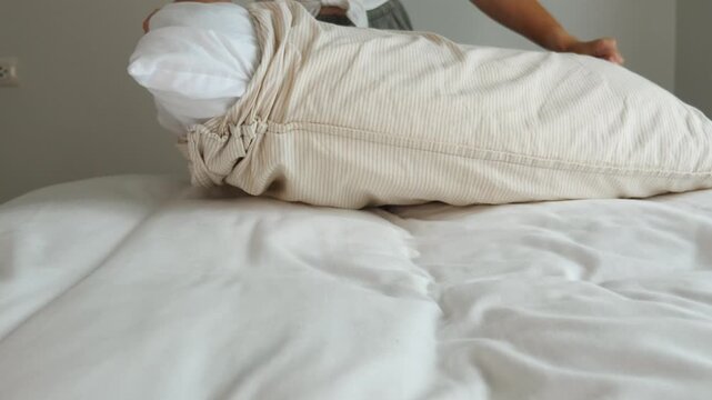 Hands removing white pillow from striped pillowcase on bed with white linens, domestic chore, laundry day, home maintenance, lifestyle .