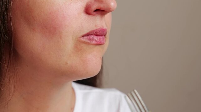 A person takes a bite of broccoli from a fork. The focus is on the mouth and cheek as the person enjoys the food. The setting shows a simple background