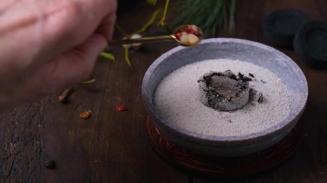 Incense burning on glowing charcoal with dark background - placing incense with a spoon