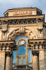 Naklejka premium Moscow, Russia - May 21, 2026: Historic bank building showcasing intricate stone architecture, large windows, and a clock, with the word BANK prominently displayed