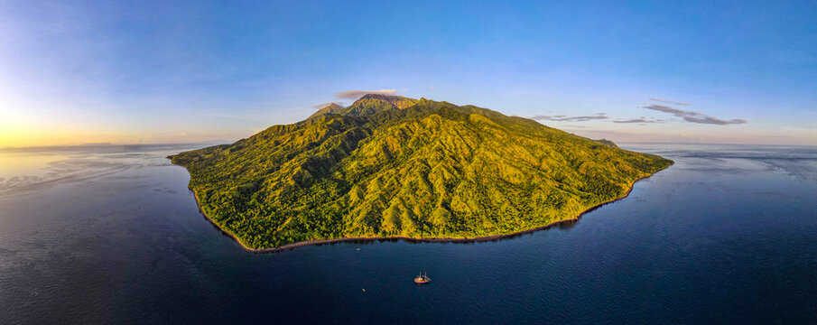 Aerial view of Komodo National Park featuring lush green mountains and rugged terrain surrounded by deep blue sea at golden hour in East Nusa Tenggara, Indonesia.