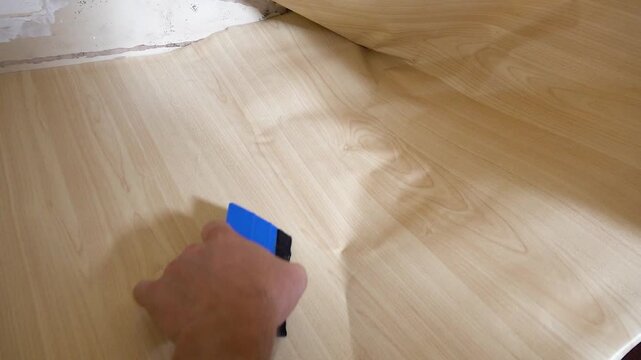 Close up view of a person using a squeegee to apply self-adhesive vinyl film onto a cabinet surface under a sink during home renovation.