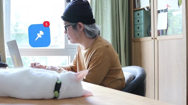 Side view of a mature Asian man with long white hair and glasses using a laptop at home next to his white cat, with a 3D tracked pushpin board note notification pop up and red counter.