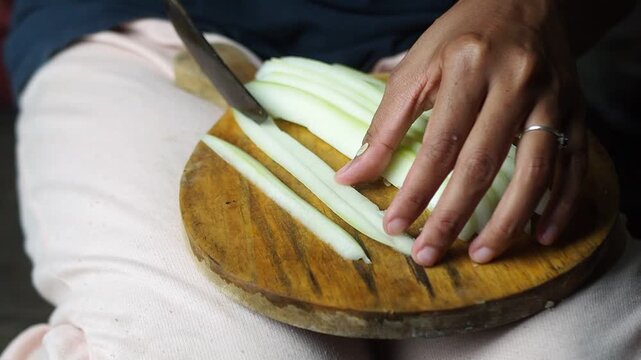 Close-up of a person's hands slicing fresh green papaya into thin strips on a wooden cutting board, preparing a healthy meal