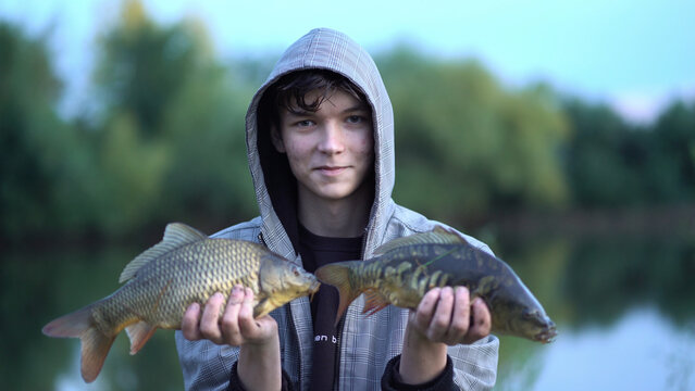 fisherman holding two carp, showing his catch to the camera